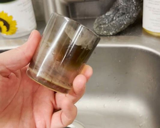 A hand holding a glass votive candle holder covered in soot
