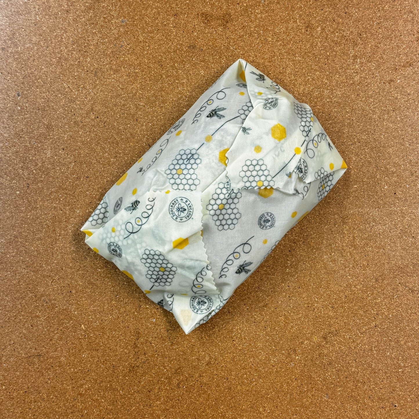 Folded beeswax wrap around a large loaf of bread with honeycomb and bee pattern on a brown surface