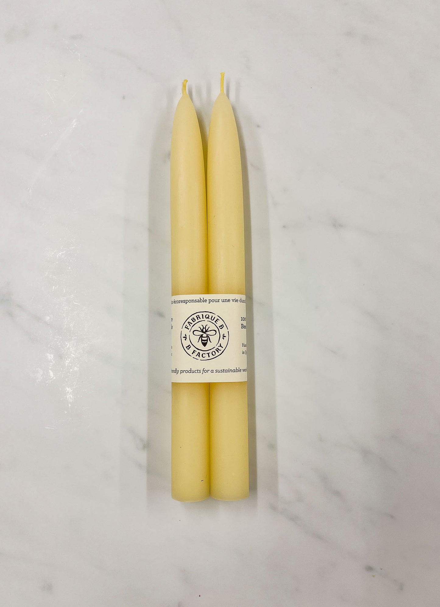 Set of 2 handmade beeswax taper candles wrapped in cardboard ring packaging with B Factory logo
