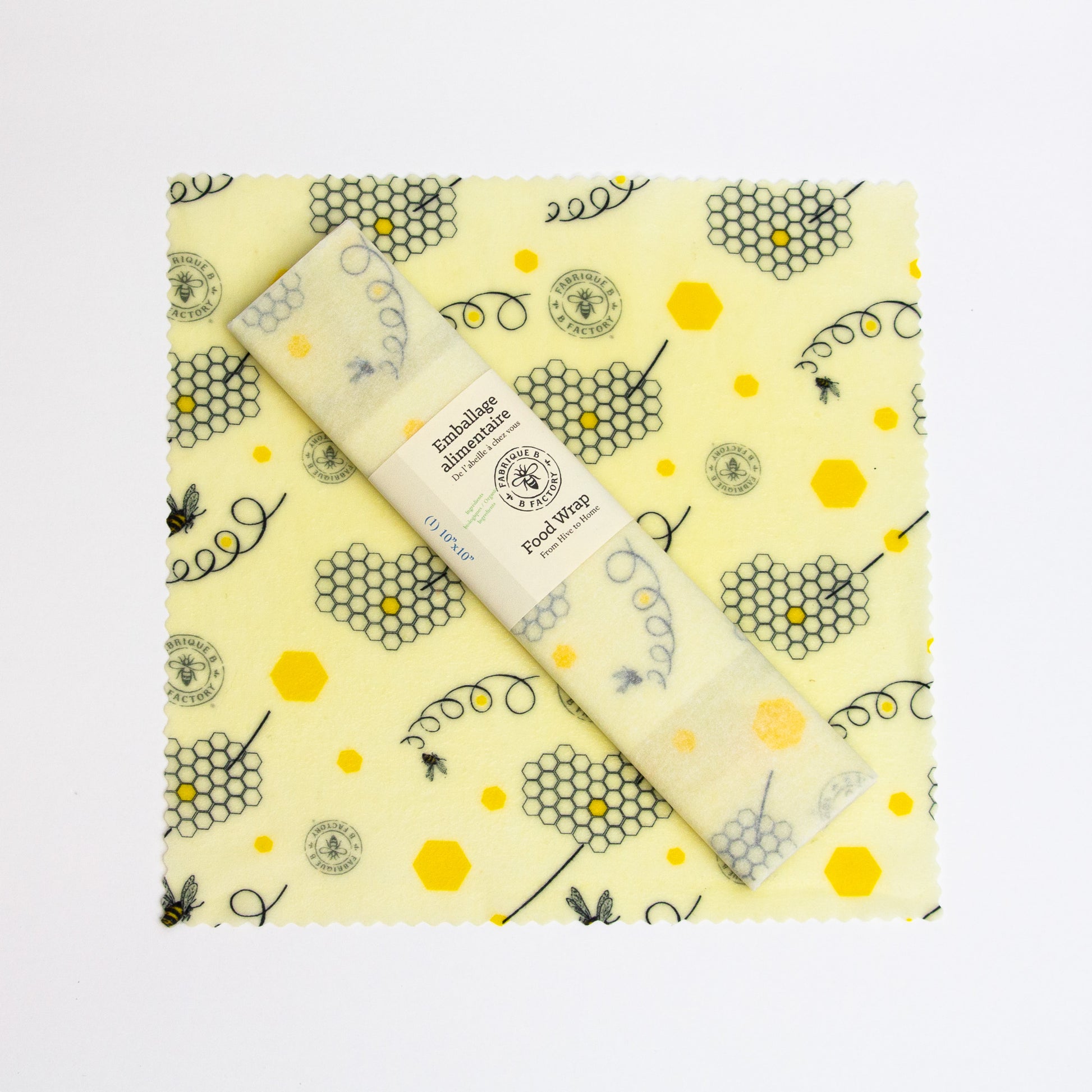 A 10-inch square patterned beeswax food wrap with honeycomb and bee design and a wrapped beeswax wrap sitting on top with B Factory logo