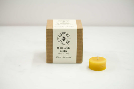 Single pure beeswax tea light candle next to cardboard box that says B Factory 12 tea lights refills without cups 100% beeswax