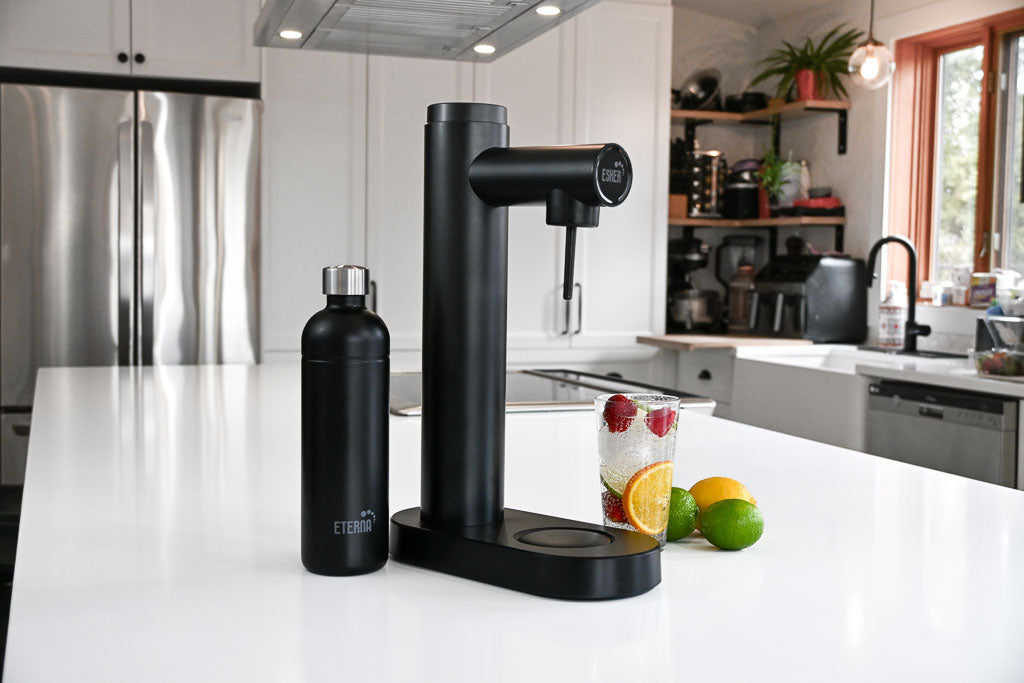 Black Esker soda making machine and Eterna black stainless steel bottle on a white countertop with a modern kitchen background