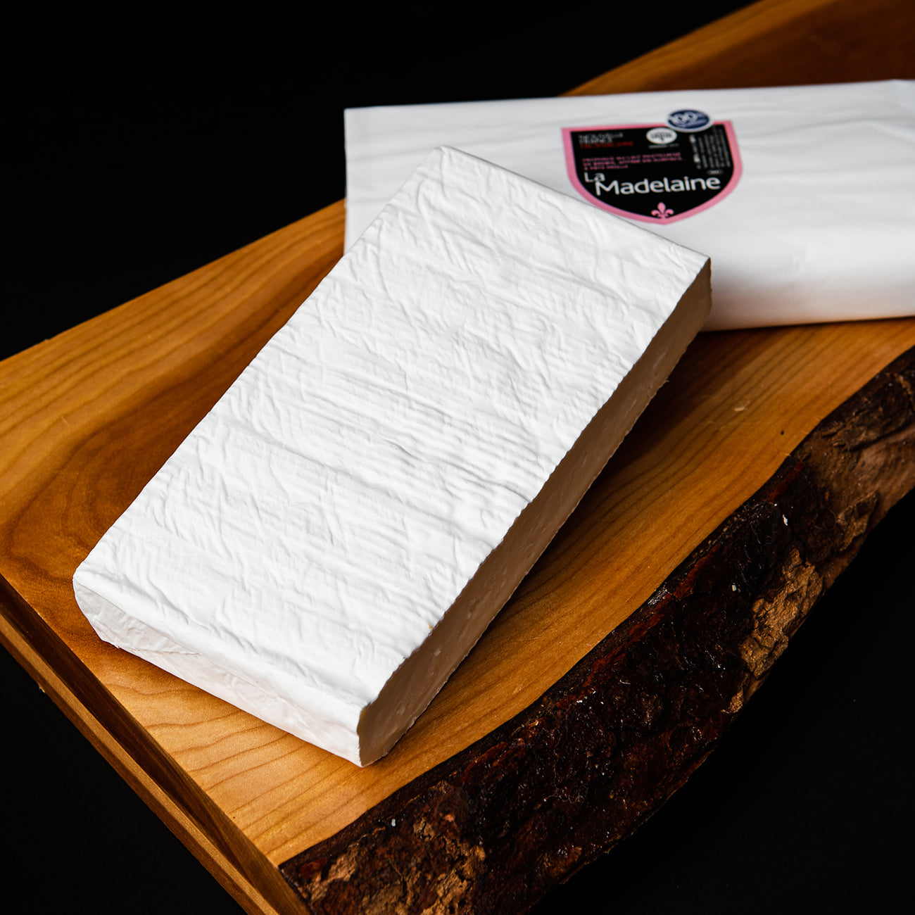A wheel of Fromagerie Nouvelle France La Madelaine cheese, featuring a soft, creamy interior and a delicate rind, presented in branded packaging.