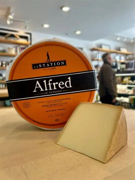 A wheel of Fromagerie La Station organic Alfred Le Fermier cheese, featuring a firm texture with a natural rind and golden interior.