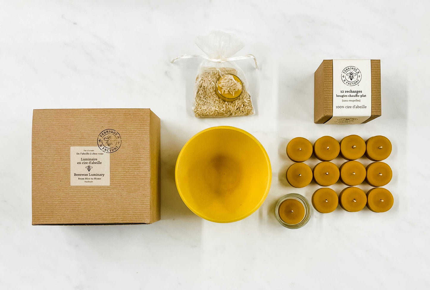 Top view of large B Factory gift box next to eco-friendly luminary, 12 tea light beeswax candles, pack of rice, small B Factory gift box
