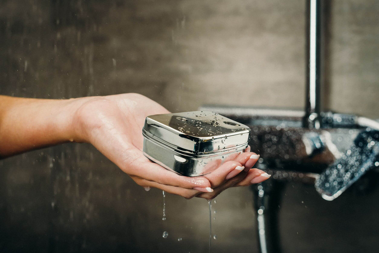 Hand holding wet food-grade stainless steel soap dish under running shower header