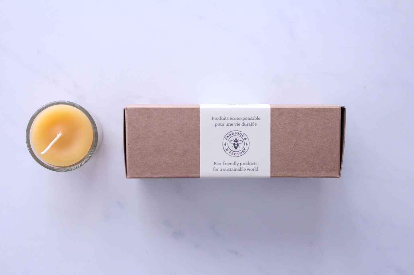 Pure beeswax votive candle in glass holder beside 3 beeswax votive candles in gift box with B Factory logo on lid