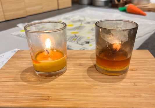 2 lit votive candles in glass holders: one candle holder is clean, the candle holder other is covered in soot