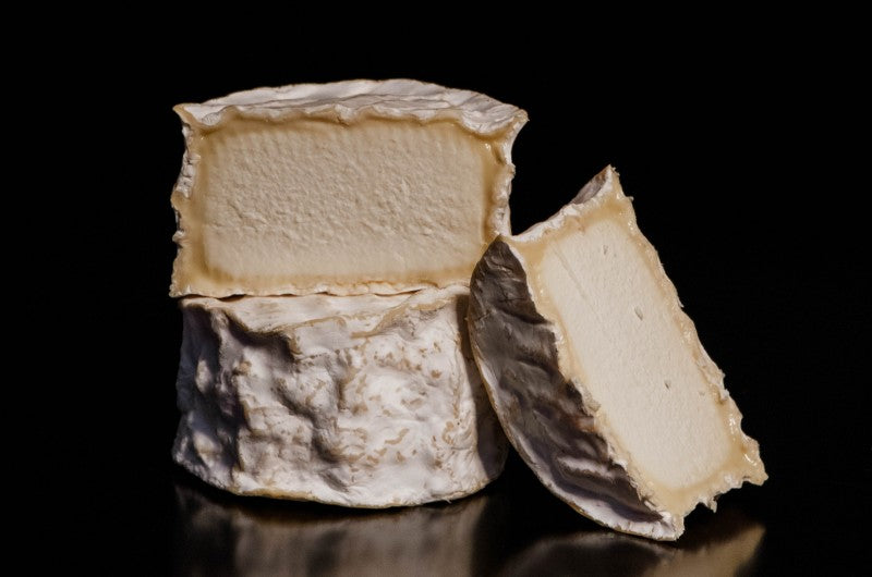 A soft-ripened cheese wheel cut in half with a creamy interior and bloomy rind