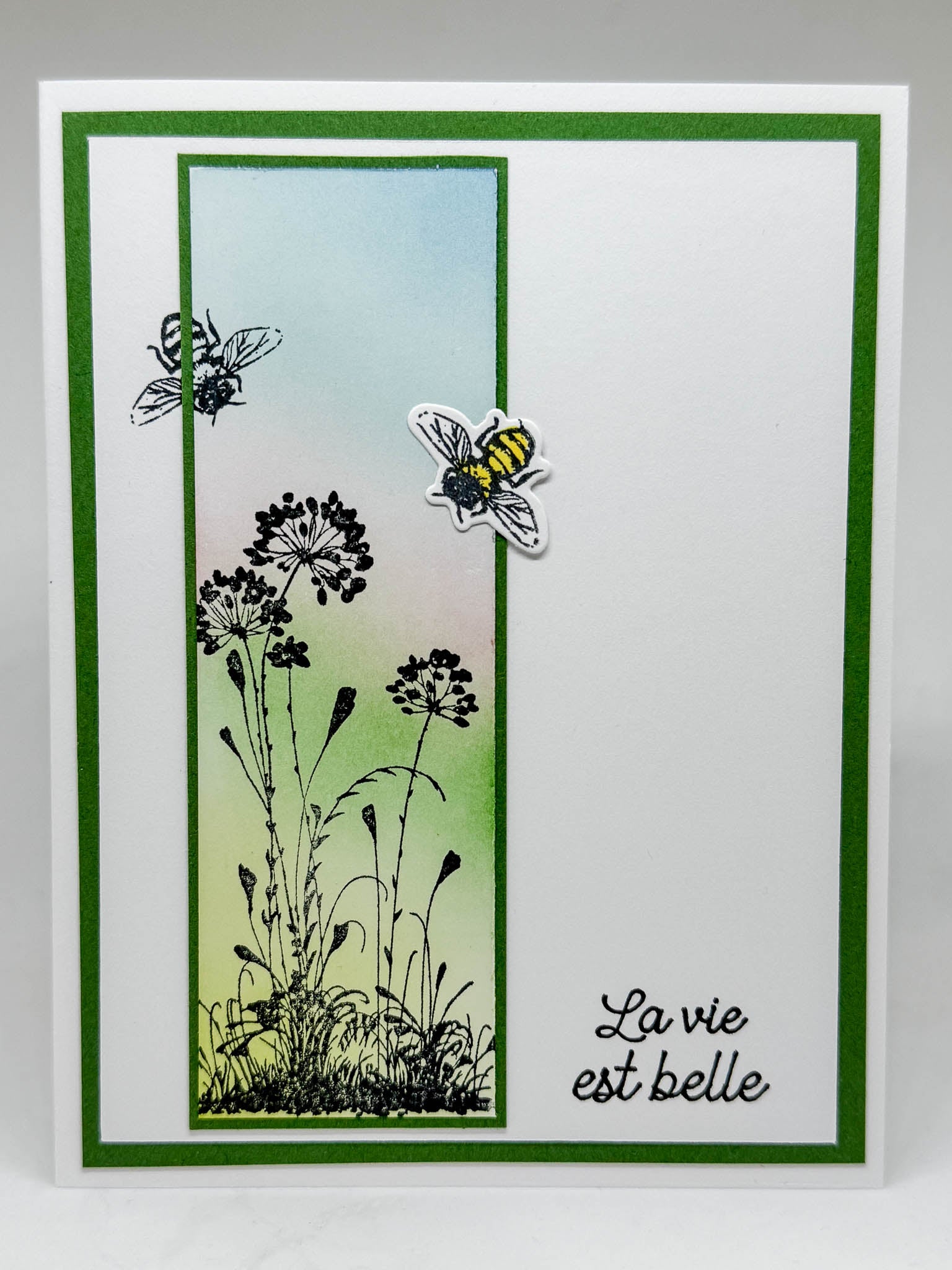 Handmade greeting card, white with a green border, flowers and bees on front and "La vie est belle" stamped at the bottom right of card