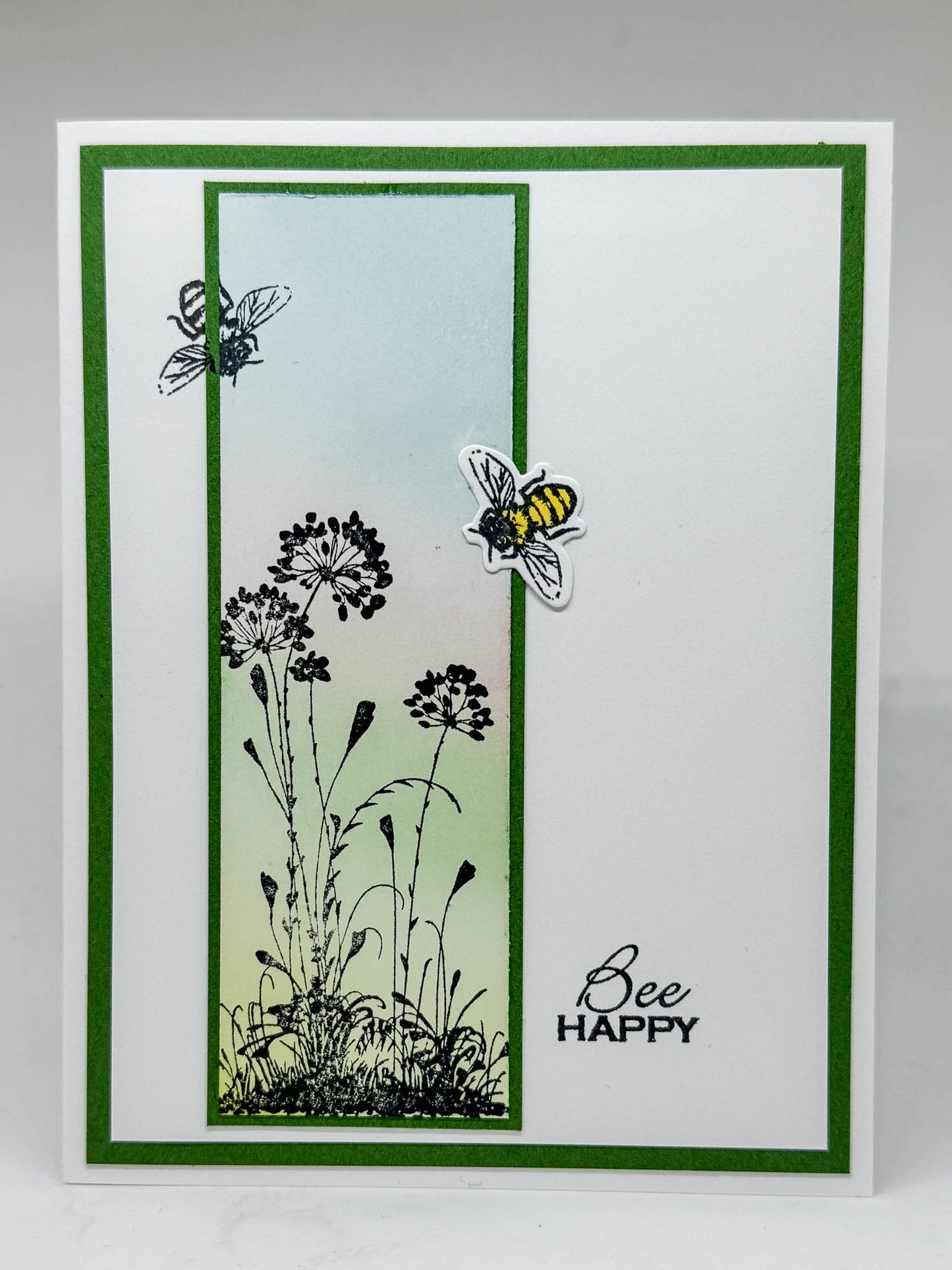 Handmade greeting card, white with a green border, flowers and bees on front and "Bee Happy" stamped at the bottom right of card