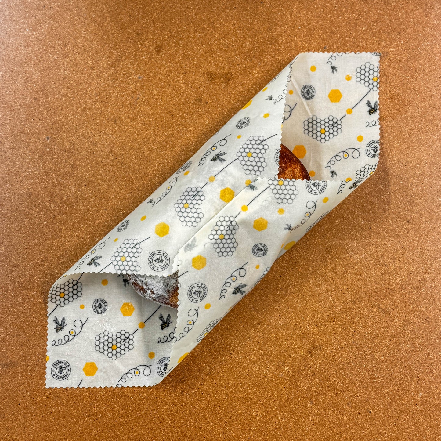 A loaf of bread rolled in a beeswax wrap with honeycomb and bee pattern on a brown surface