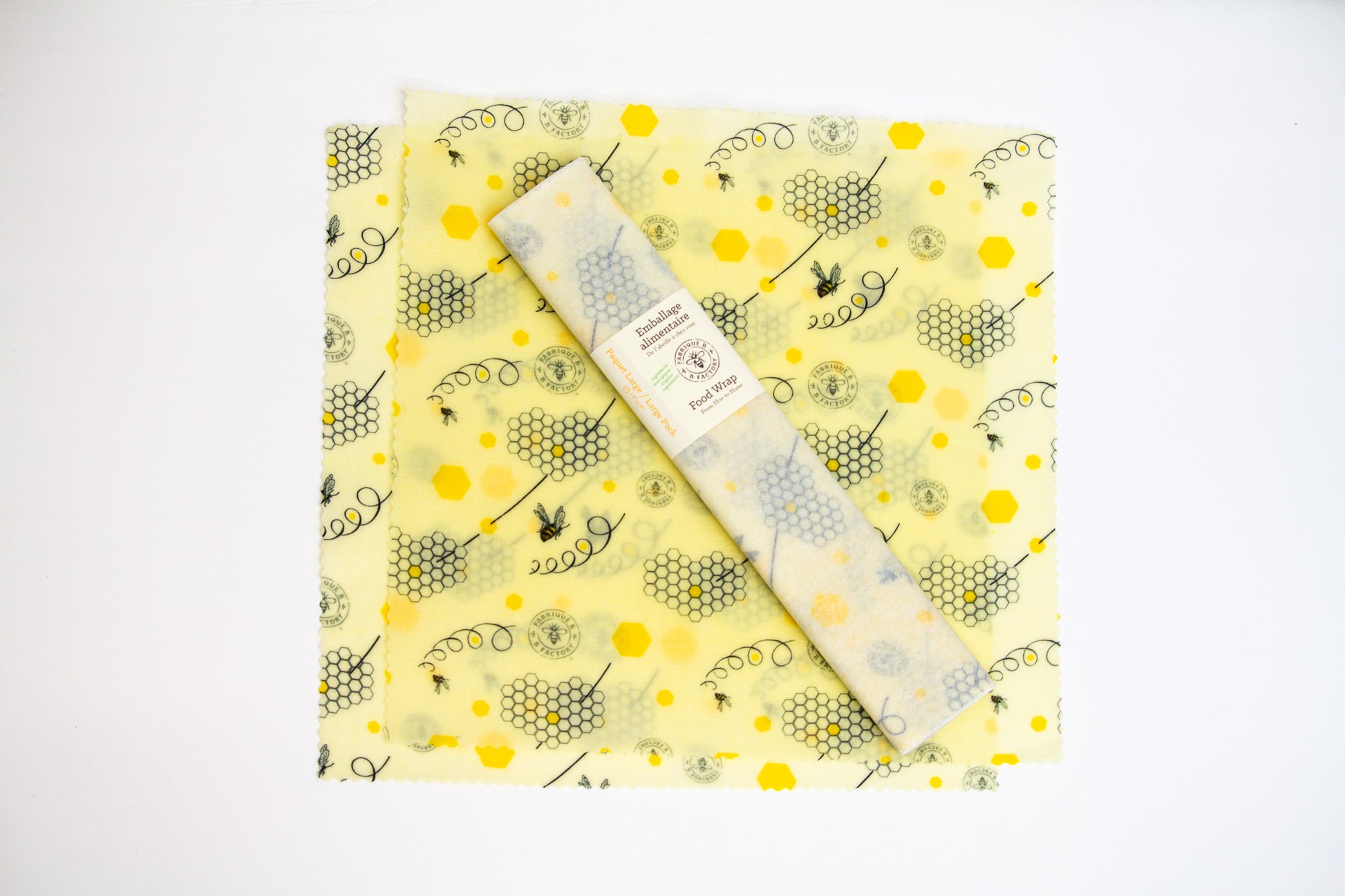 2 beeswax food wraps with honeycomb and bee pattern, with a wrapped set of 2 large beeswax wraps with B Factory logo sitting in middle