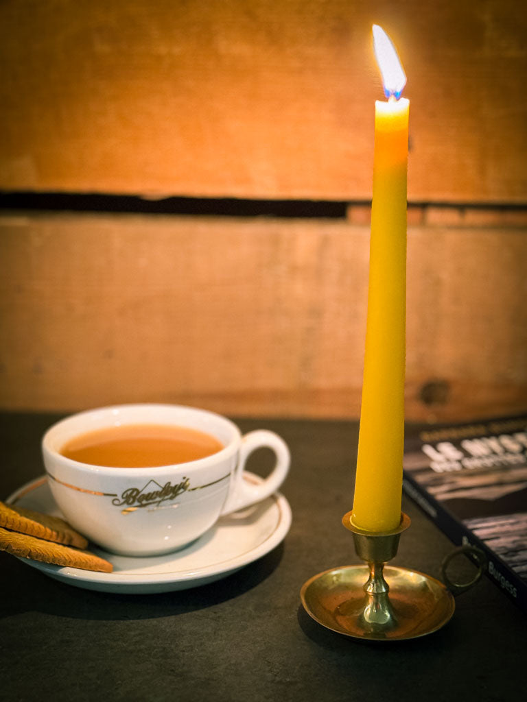 A yellow beeswax taper andle and tea cup on a table with a warm glow