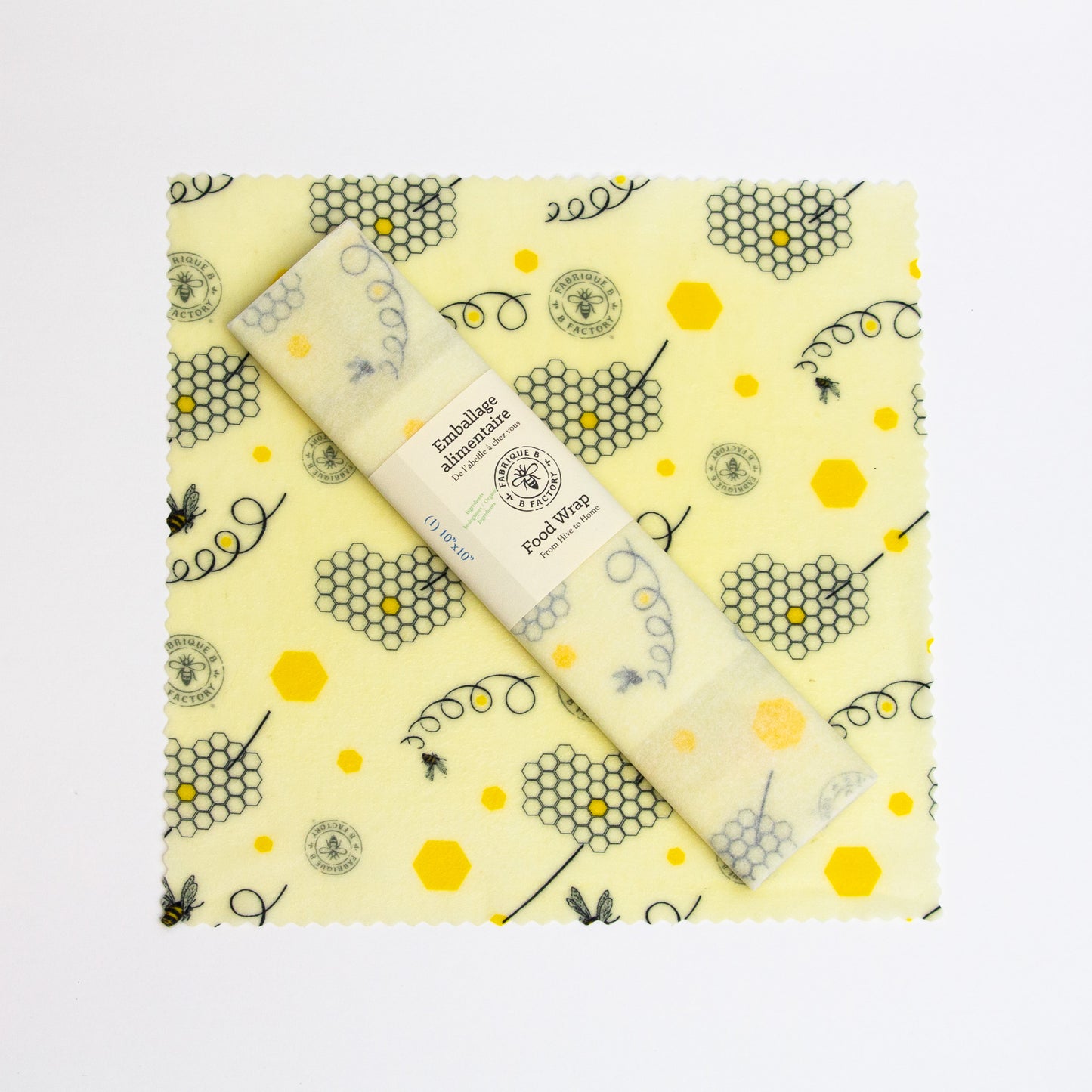A 10-inch square patterned beeswax food wrap with honeycomb and bee design and a wrapped beeswax wrap sitting on top with B Factory logo