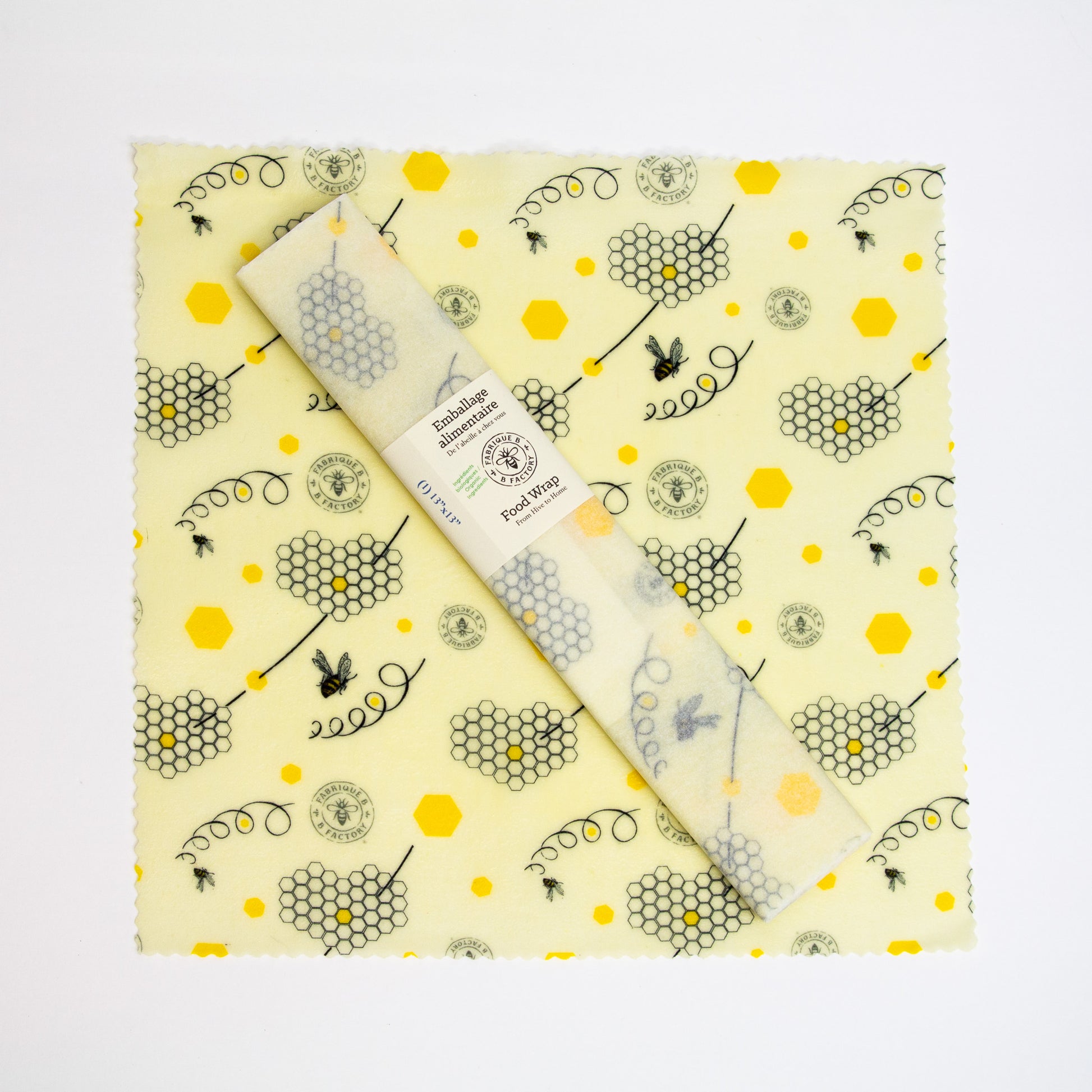 A 13-inch square patterned beeswax food wrap with honeycomb and bee design and a wrapped beeswax wrap sitting on top with B Factory logo