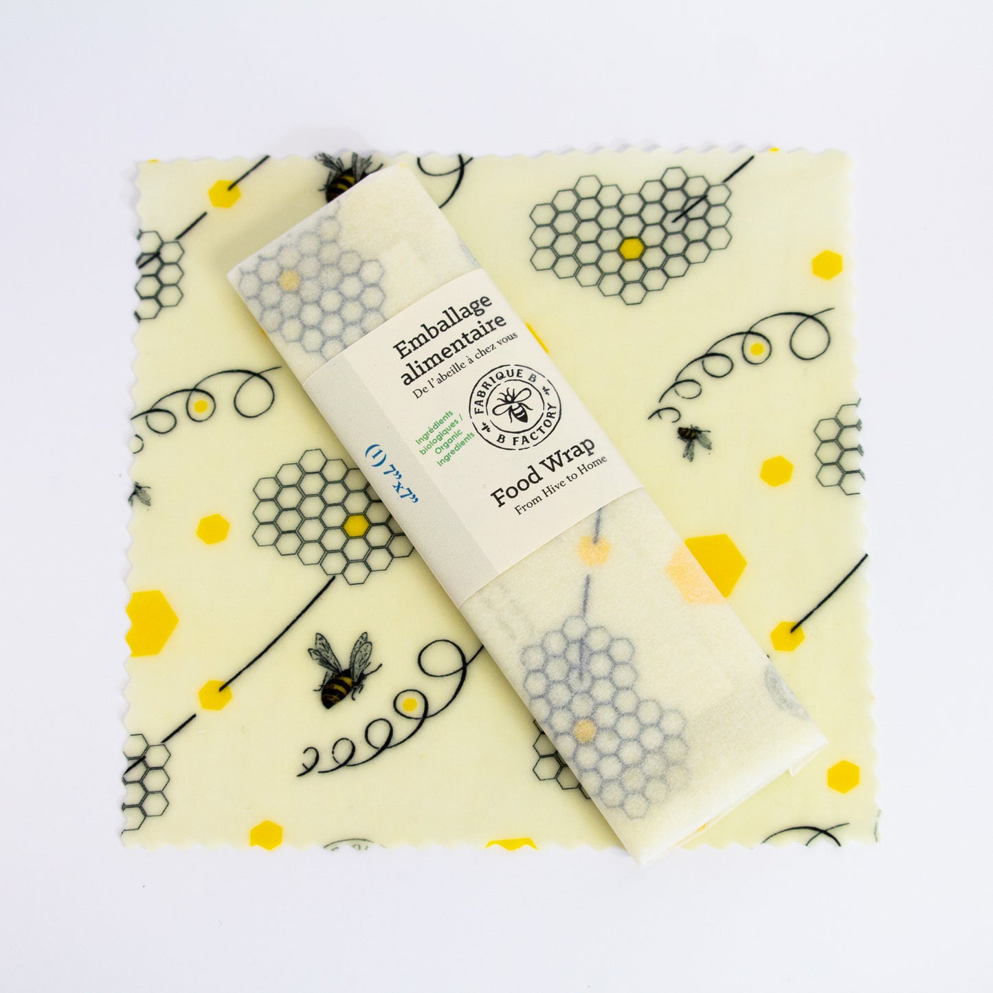 A 7-inch square patterned beeswax food wrap with honeycomb and bee design and a wrapped beeswax wrap sitting on top with B Factory logo