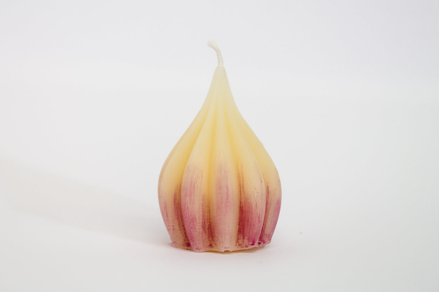 One large garlic-shaped beeswax candle with purple tint on white background