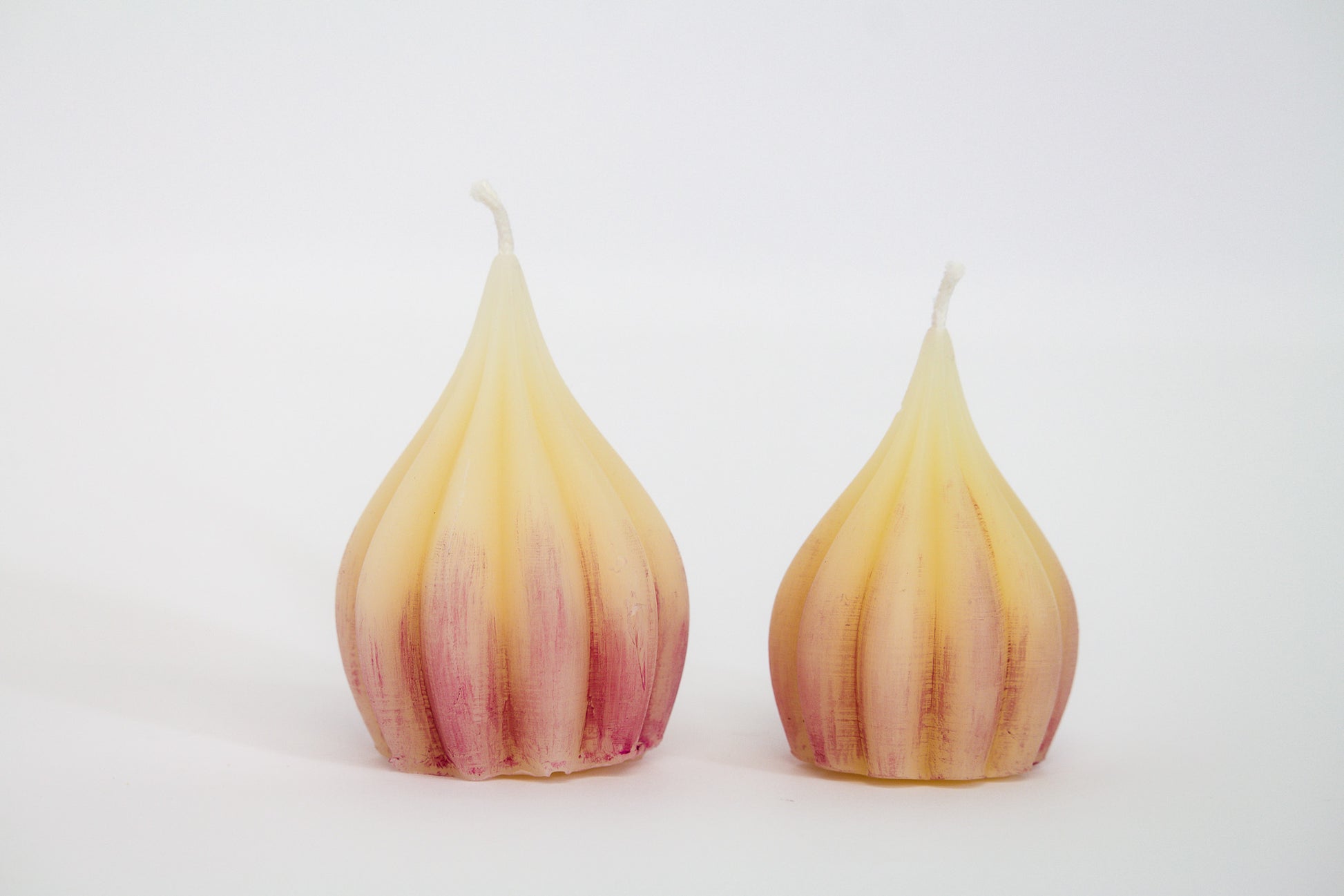One large and one small pure white beeswax candle with purple tint on white background