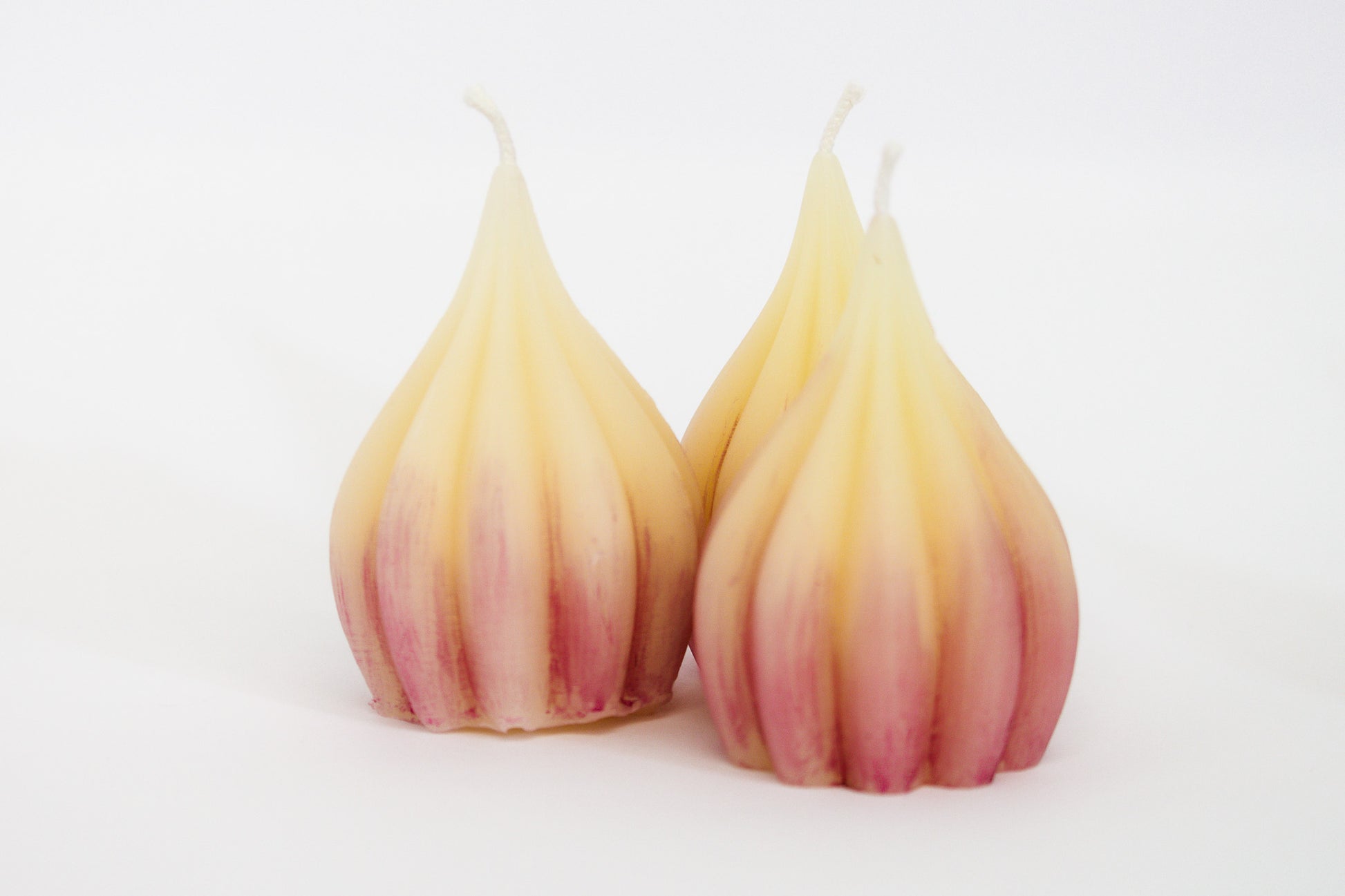 Group of three white pure beeswax garlic-shaped candles with purple tint on white background