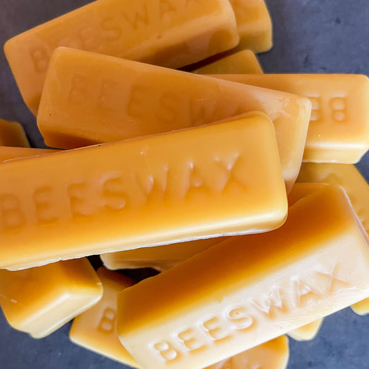 Jumbled pile of golden yellow beeswax bars, "beeswax" is written on each bar