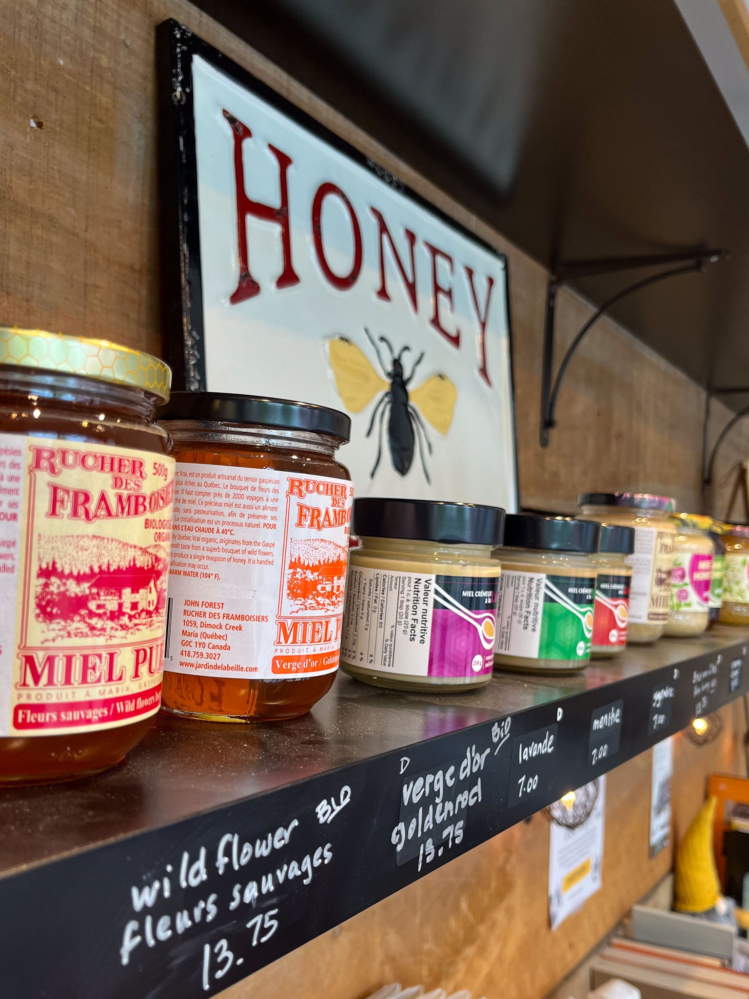 A shelf full of jars of Quebec honey with a "honey" sign on the shelf behind the honey