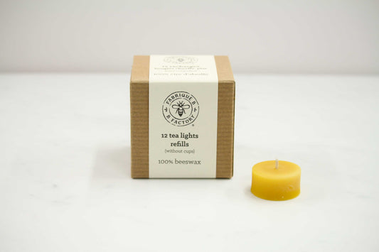 Single pure beeswax tea light candle next to cardboard box that says B Factory 12 tea lights refills without cups 100% beeswax
