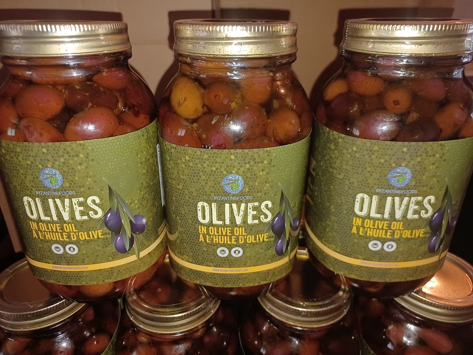 Three jars of olives with green labels on a shelf.