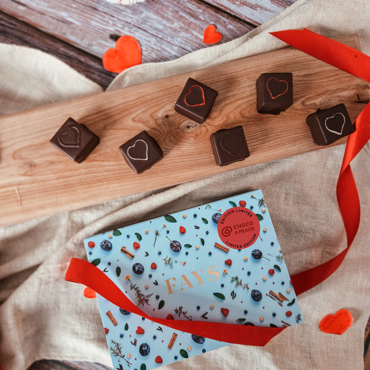 FAYS artisanal chocolates displayed on a wooden board, featuring heart-shaped designs on each piece, with decorative red ribbons and gift-style packaging in the background.
