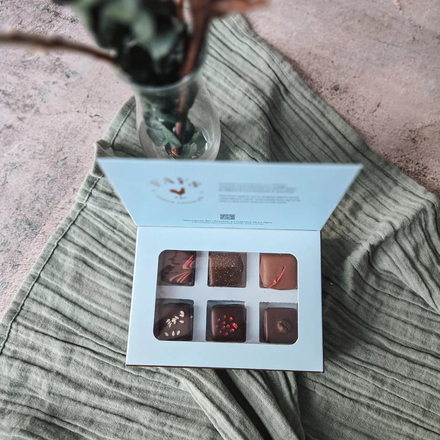 Open box of chocolates on a textured surface with a plant in the background