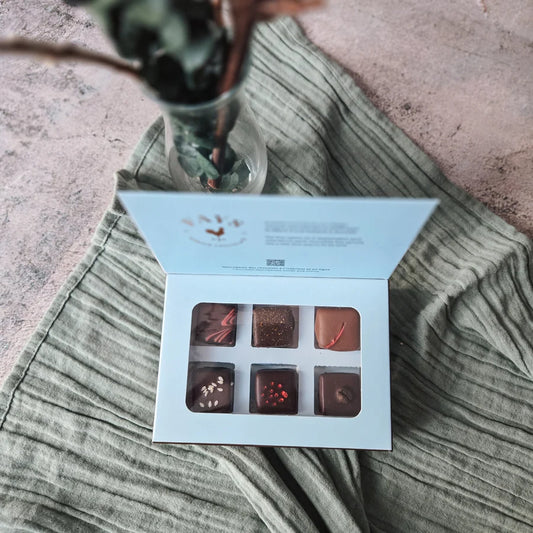 Open box of chocolates on a textured surface with a plant in the background