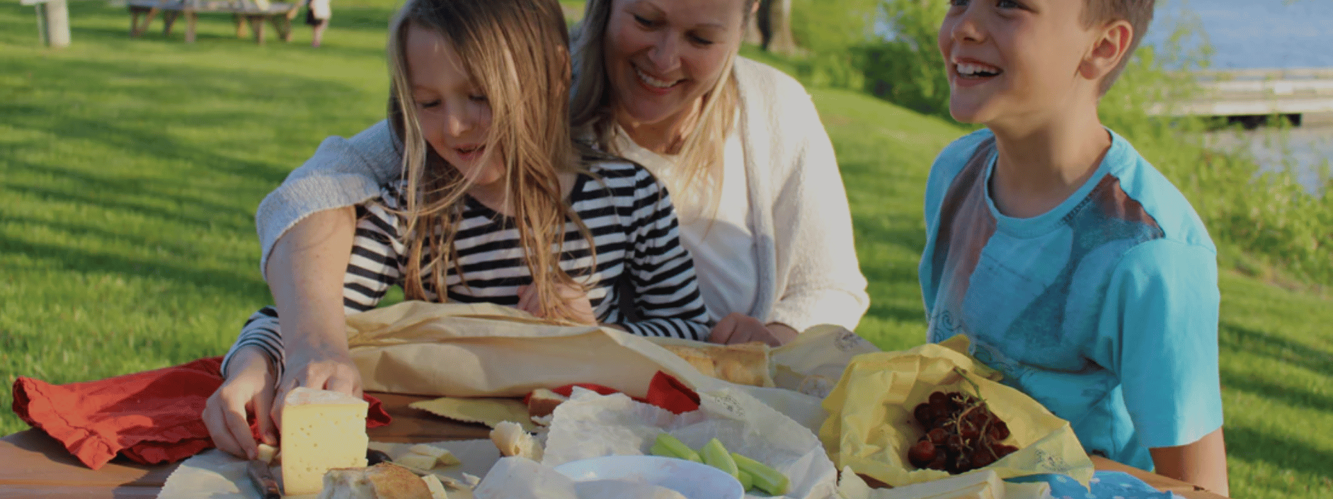 Mother with son and daughter smiling at a picnic table with cheese and fruits wrapped in beeswax wraps