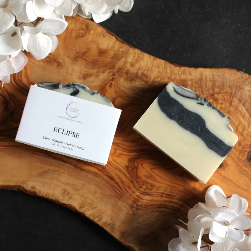 Black and white bar soap "Eclipse" by Hudson Soap Company on a wood table  with white flowers in the corner