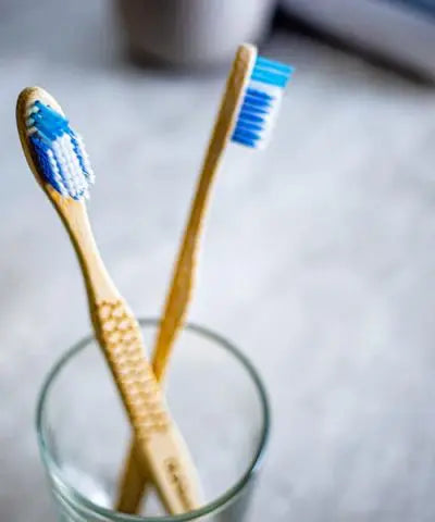 2 bamboo toothbrushes in a clear glass cup, with blue and white bristles