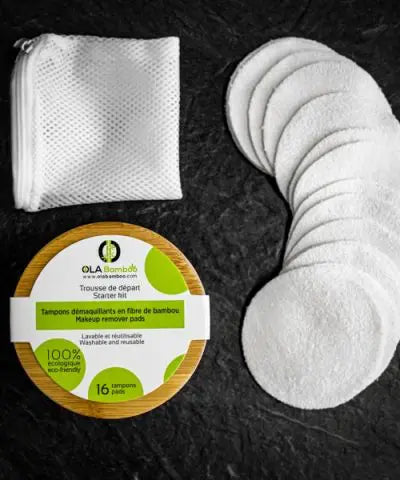 A mesh bag, a round bamboo box seen from the top, and a column of makeup remover pads set on a slate grey surface