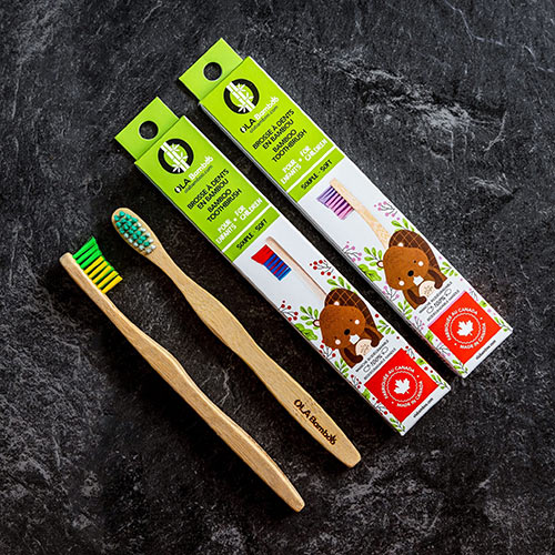 2 boxes of kids bamboo toothbrushes by Ola Bamboo, with toothbrushes to the left side of the boxes