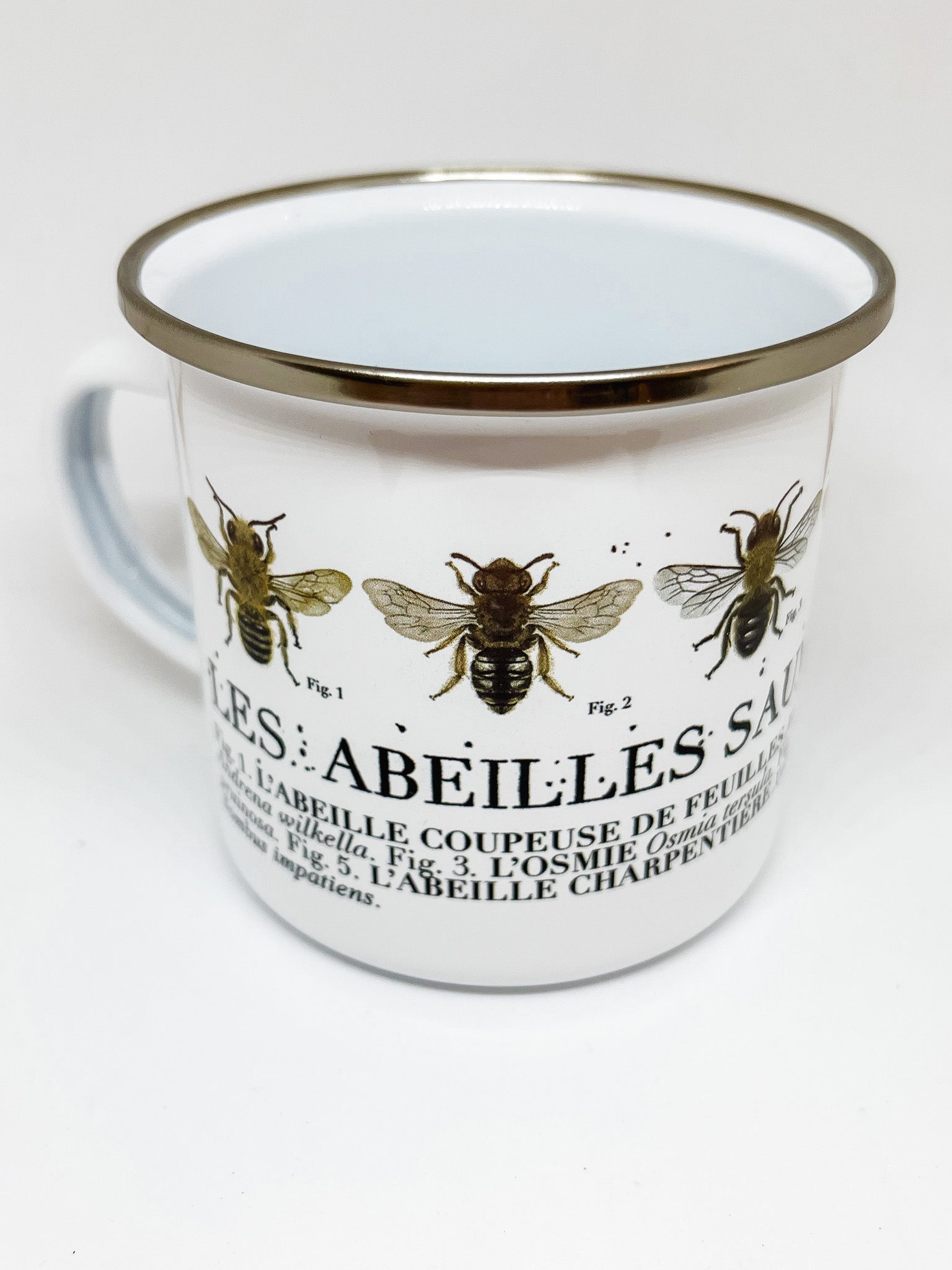 White enamel mug with silver rim and illustrations of wild quebec bees with text below identifying each bee. Figures 1 and 2 visible