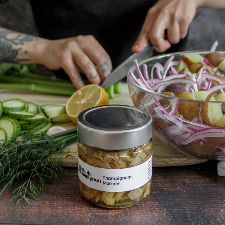 A jar of Les 400 Pieds de Champignon pickled mushrooms, featuring whole mushrooms preserved in a tangy brine.