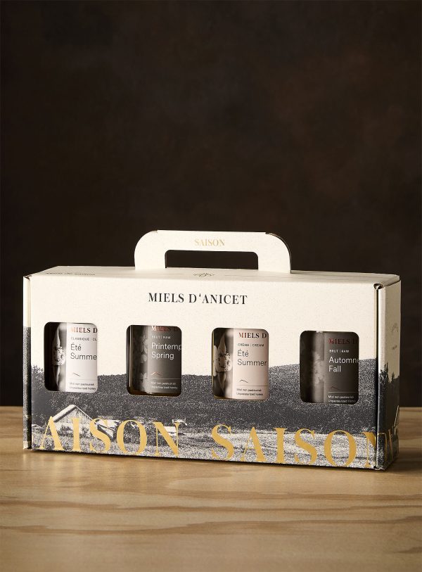 Packaging of Miel d'Anicet honey with four jars on a wooden surface and dark background