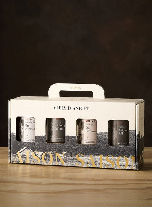 Packaging of Miel d'Anicet honey with four jars on a wooden surface and dark background