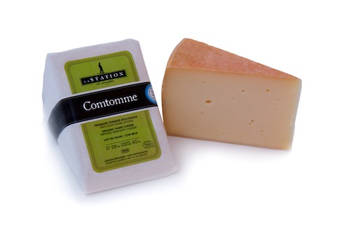 A wheel of Fromagerie La Station organic Comtomme cheese, featuring a firm texture with a natural rind and pale interior.