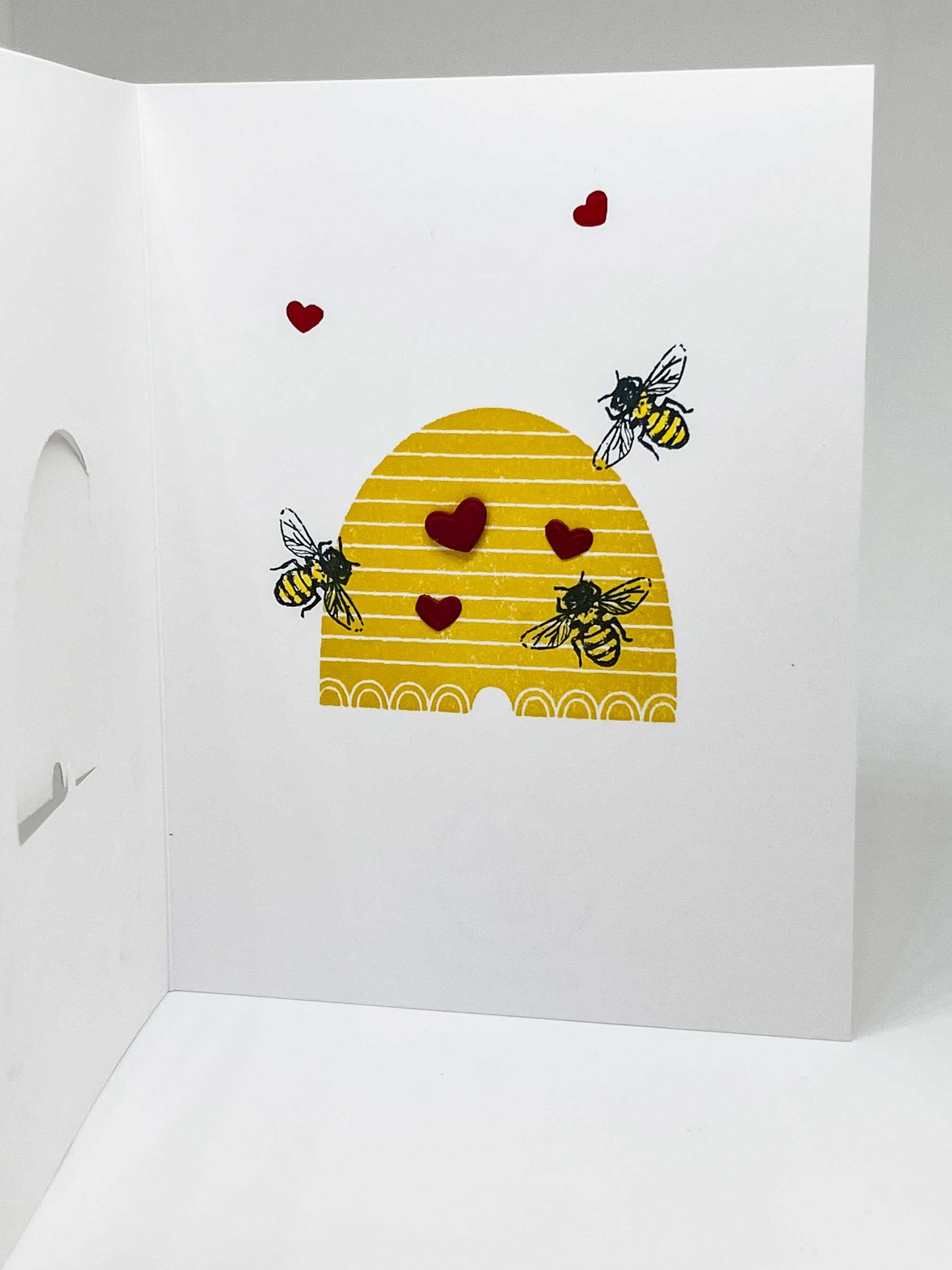 Inside pop-up greeting card with honeybees flying over hive surrounded by little red hearts