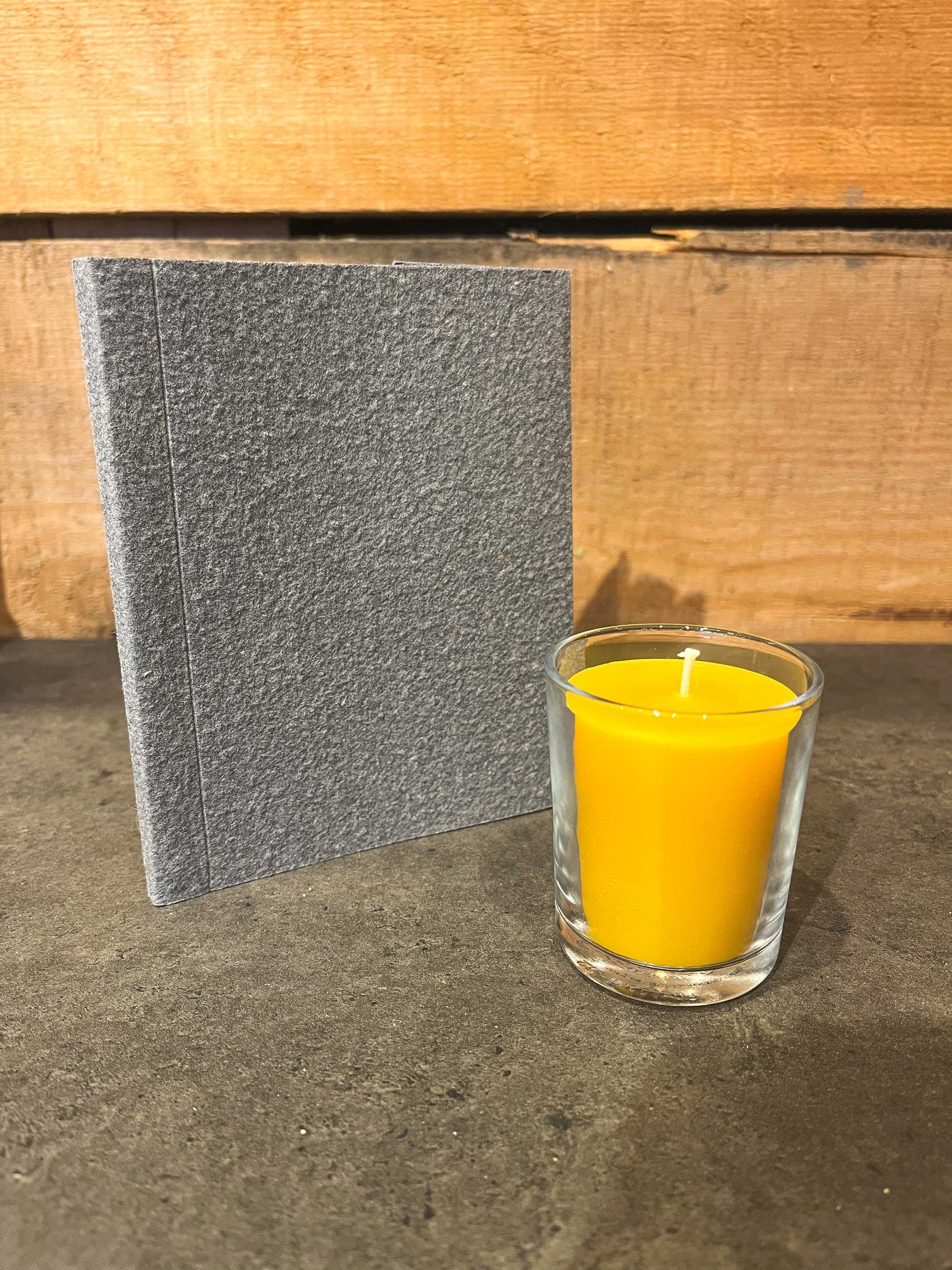Handmade beeswax votive candle in glass cup next to blue eco-friendly notebook