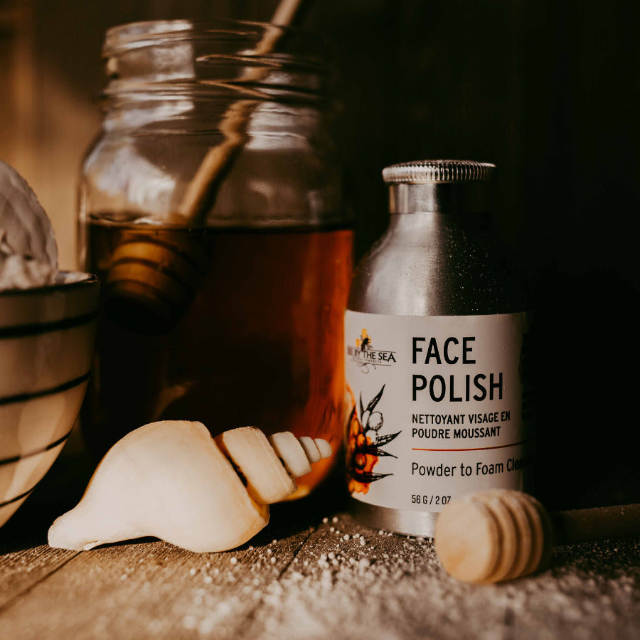 Powder to foam face cleanser in eco-friendly aluminum bottle next to jar of honey and a seashell