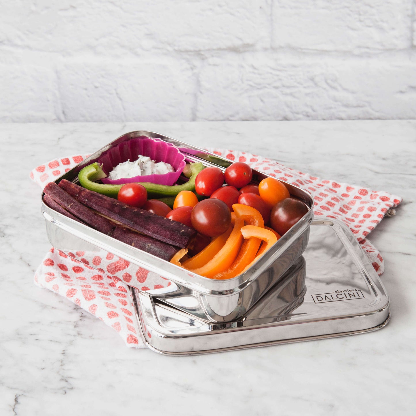 Carrots, baby tomatoes, bell peppers and dip in stainless steel food storage box