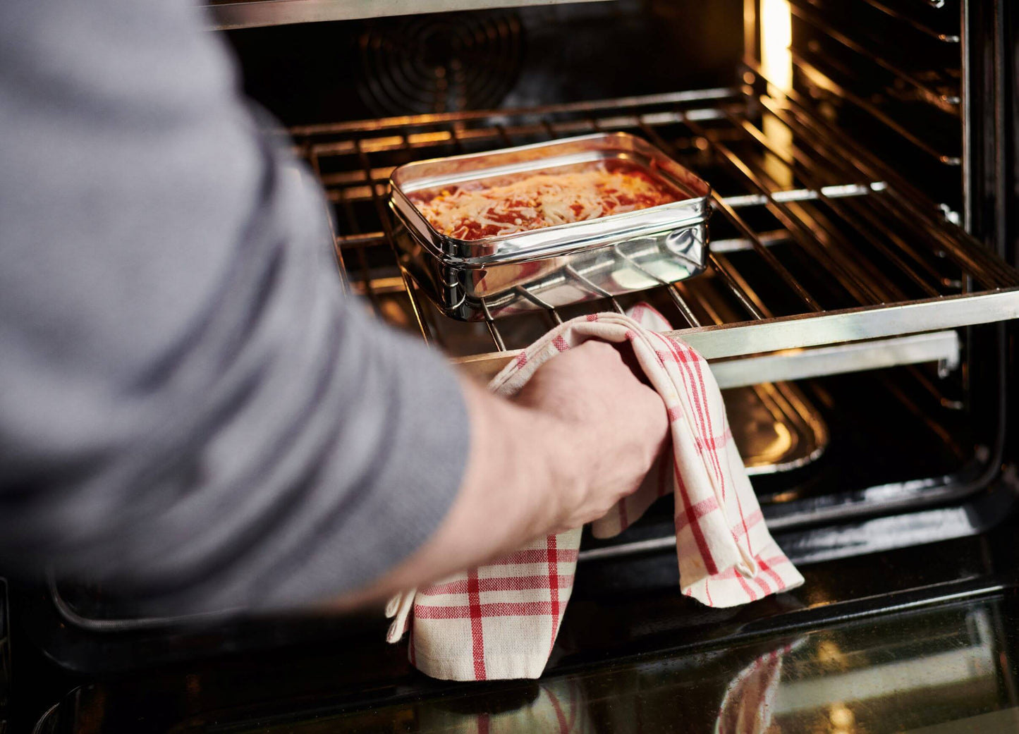 Hand putting lasagna in stainless steel food storage box inside an oven