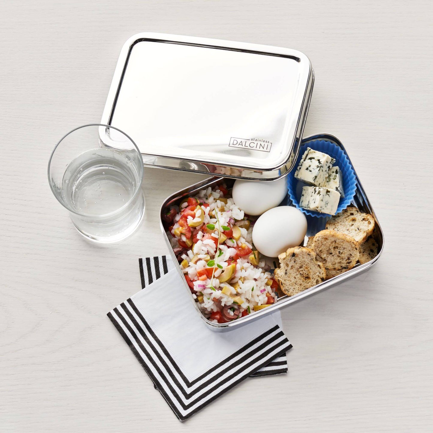 2 hard boiled eggs, crackers, cheese, and rice salad in stainless steel food storage box
