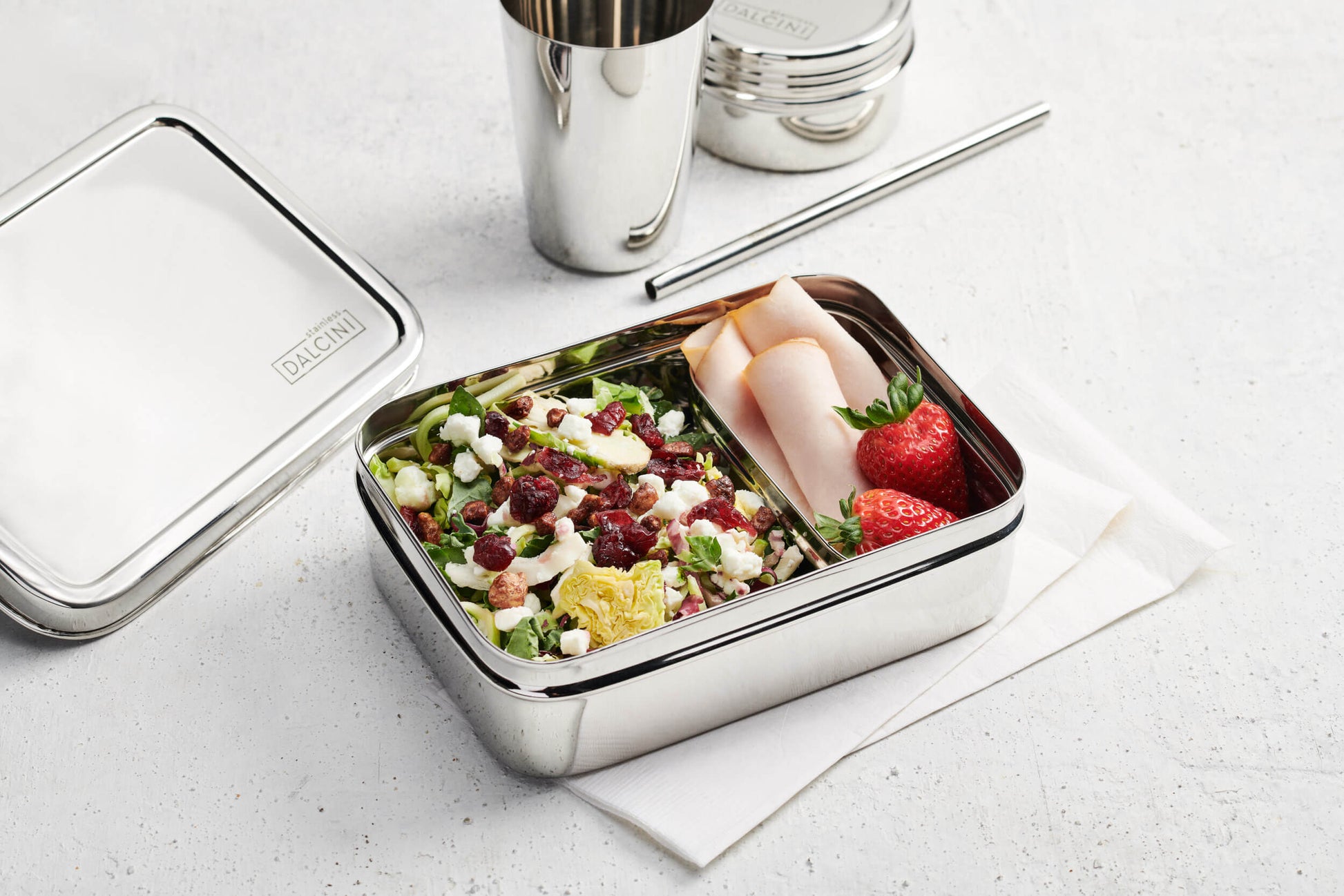 Salad, ham, and strawberries in stainless steel bento box next to stainless steel straw and tumbler
