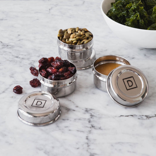 3 stainless steel condiment containers filled with dried cranberries, gravy, and pumpkin seeds
