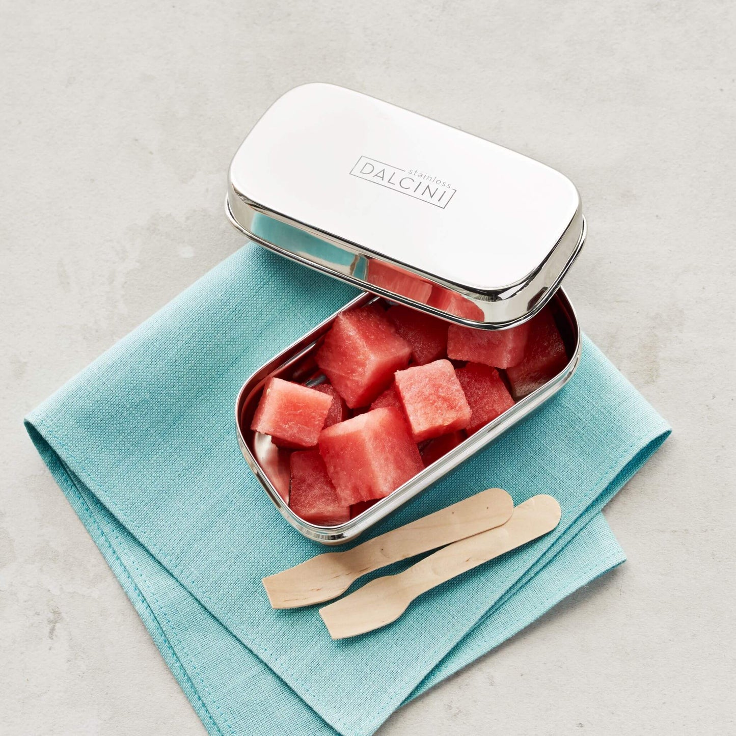 Watermelon cubes in stainless steel snack box next to wood utensils